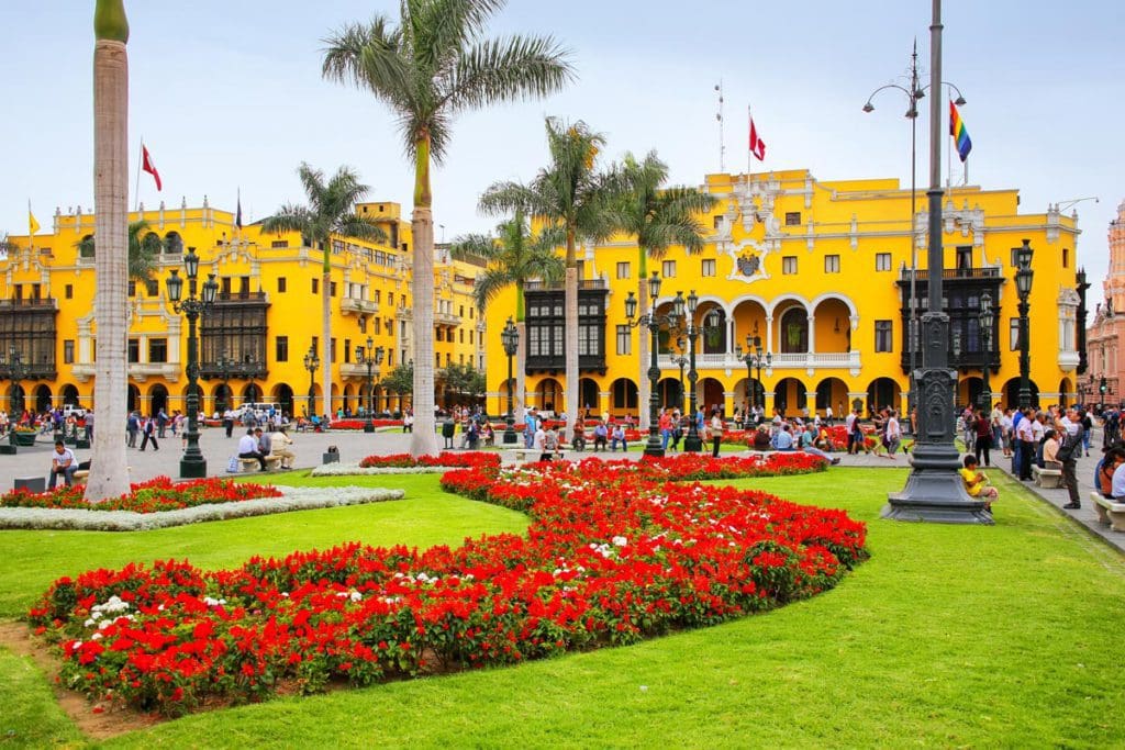 A large yellow building, with red flowers out front and swaying palm trees above them in Lima, Peru, the first stop on our Peru family vacation itinerary.