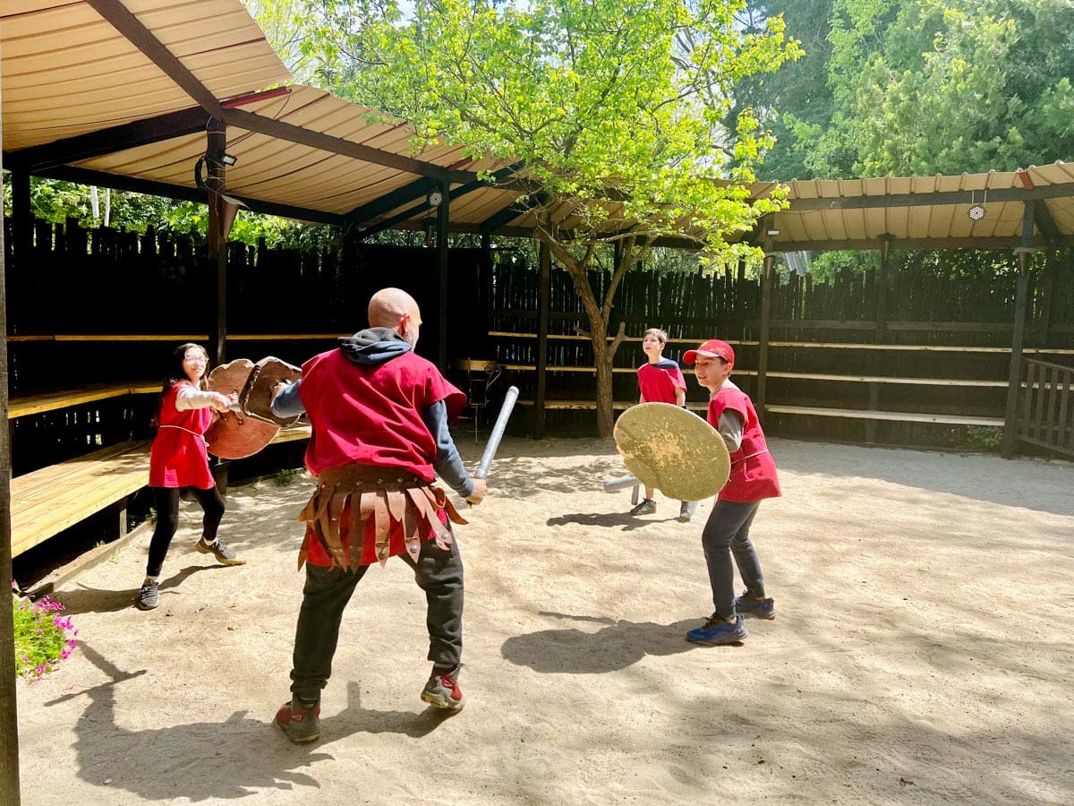 Two kids and two instructors practice gladiator fighting during a family-friendly class, a must do on our Rome itinerary with kids.