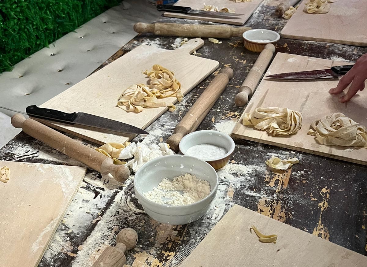 A table with supplies to make pasta, including cutting boards, flour, and small bowls.