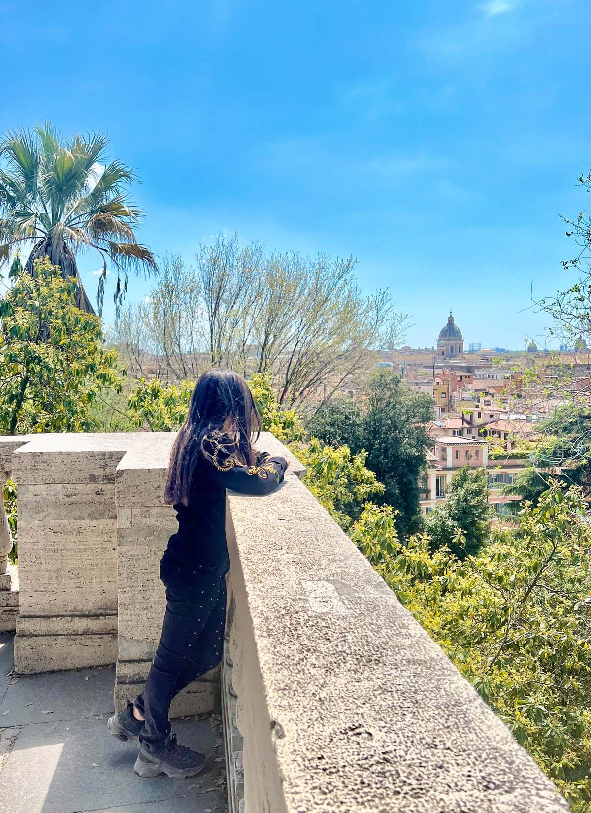 A woman leans over a wall to look at the Borghese Gardens.