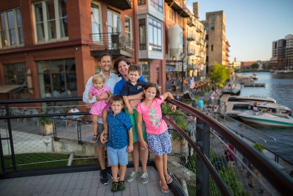 A family of five stands together on part of the Milwaukee River Walk overlooking the river, one of the best places to visit in Wisconsin for families.