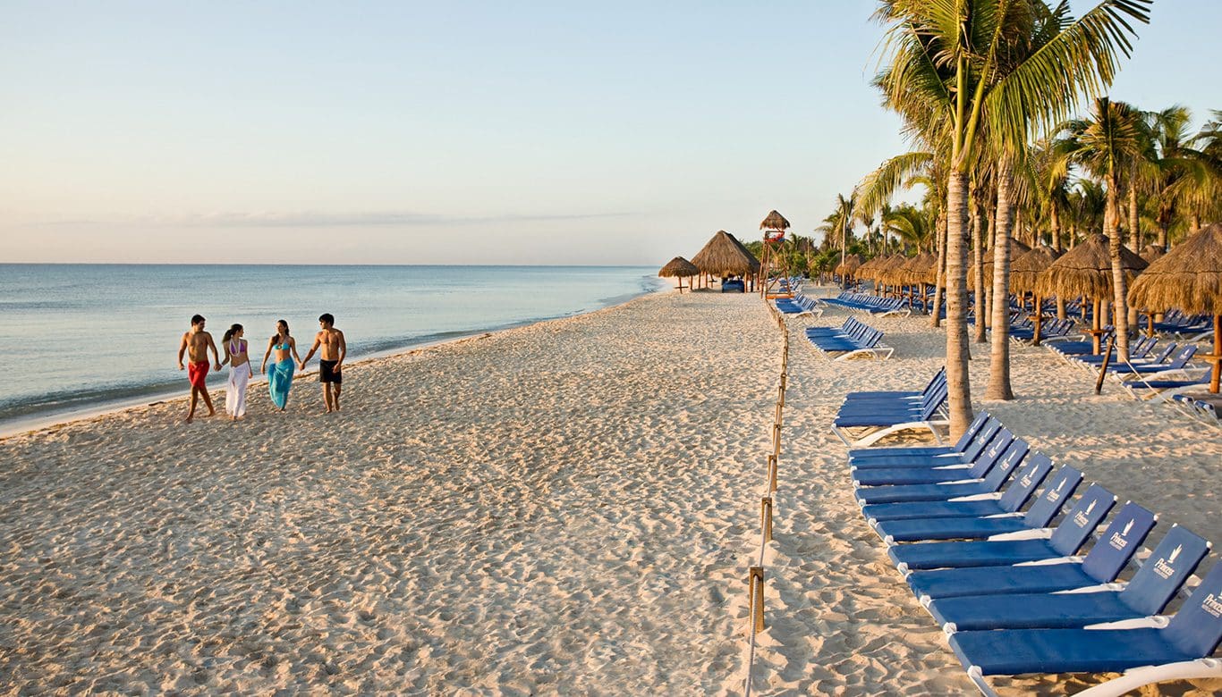 Two couples walk along the beach, lined with beach chairs, at Grand Sunset Princess, one of the best all-inclusive resorts Playa del Carmen for families.