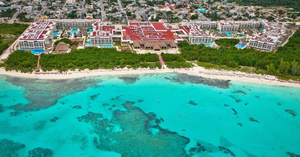 An aerial view of Paradisus Playa del Carmen Resort, featuring a long stretch of beach with resort buildings in the distance at one of the best resorts in Mexico with a water park for families.
