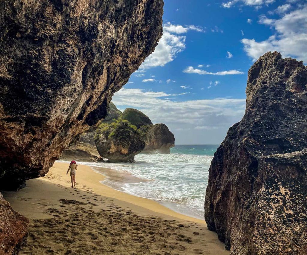 A young girl walks between huge rock formations along the beach on a sunny day at Survival Beach, a must stop on any Puerto Rico itinerary for families.