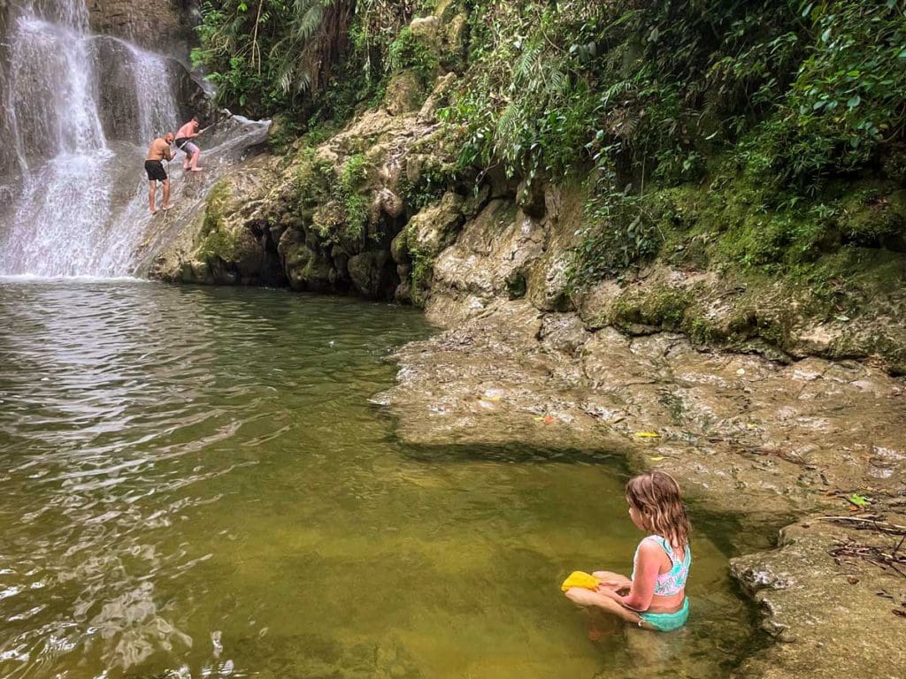 A young girl plays in the water with a small yellow bucket at Gozalandia Waterfall, a must stop on any Puerto Rico itinerary for families.