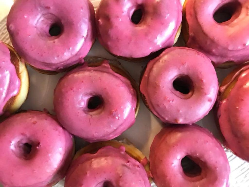 A pan filled with cherry glazed donuts at Ellē, with bright pink frosting.