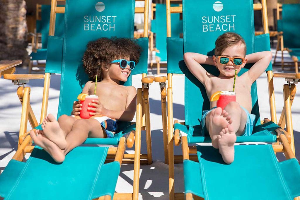 Two young boys lounging on beach chairs with a summer drink in their hands on Sunset Beach, located at the Fairmont Scottsdale Princess, one of the best luxury hotels in the U.S for families.