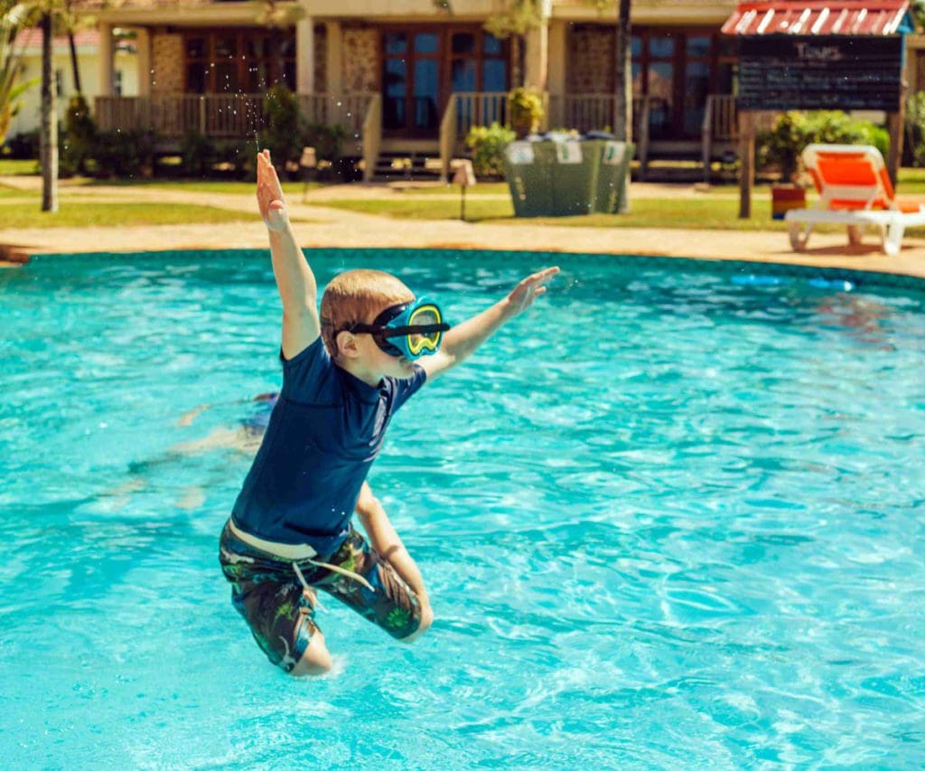 A young boy excitedly jumps into a pool, while staying at Hopkins Bay Resort, one of the best Belize resorts for a family vacation! 