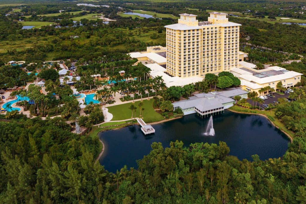 An aerial view of Hyatt Regency Coconut Point Resort and Spa, featuring a large hotel building, nearby pond, and large pool area.