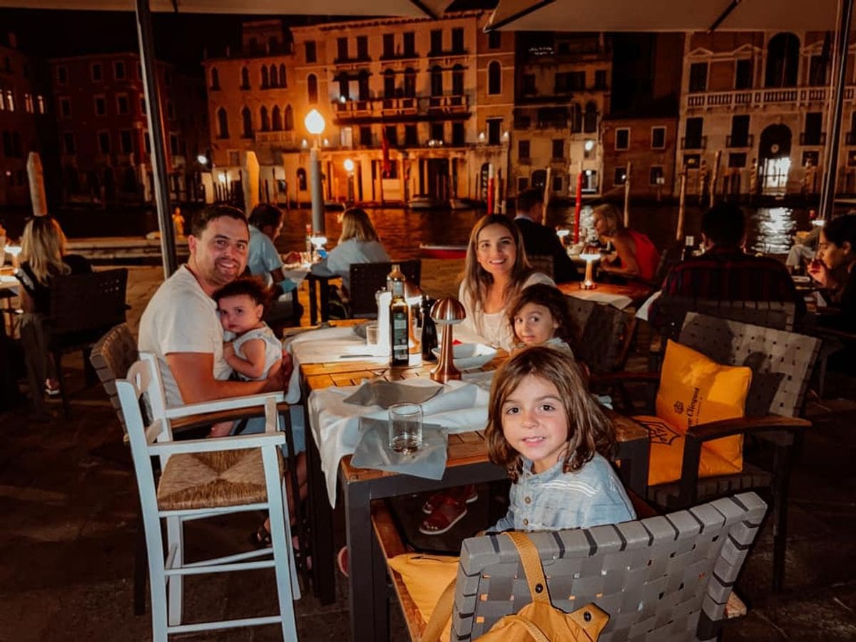 A family of five enjoys dinner at an outdoor restaurant in Venice at night.