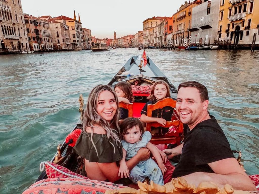 A family of five rides down a Venetian canal in a gondola.