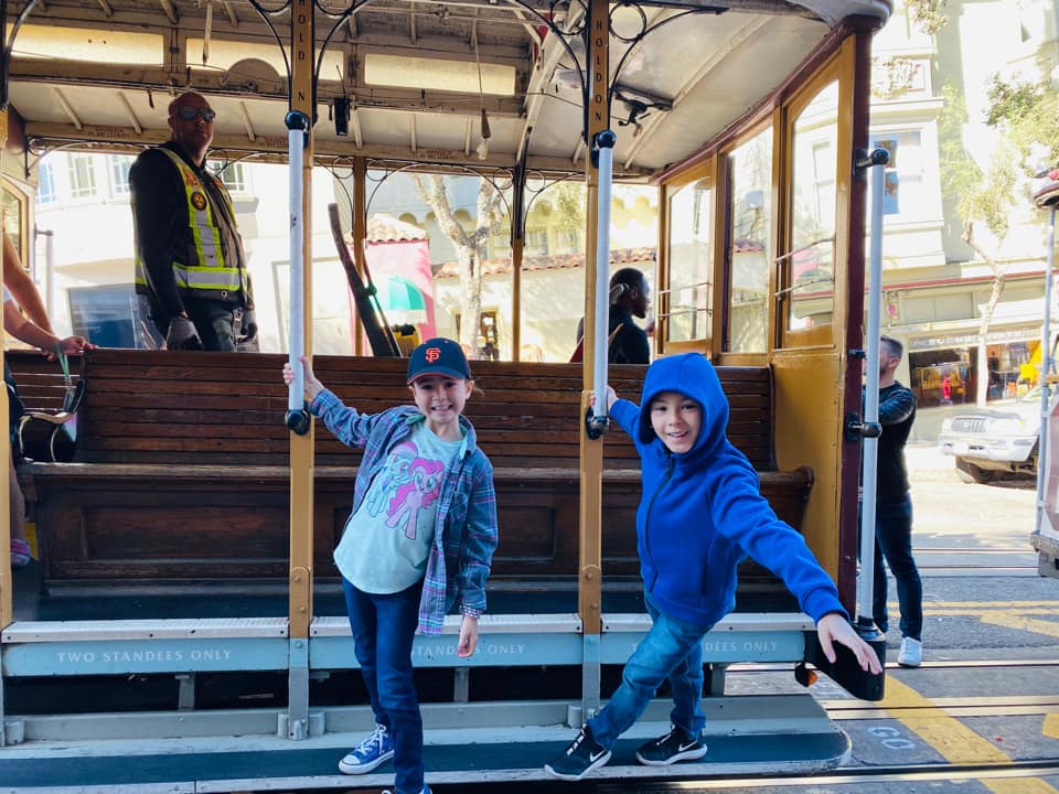Two kids hang from a San Francisco Cable Car at a museum, one of the best things to do in San Francisco with kids.