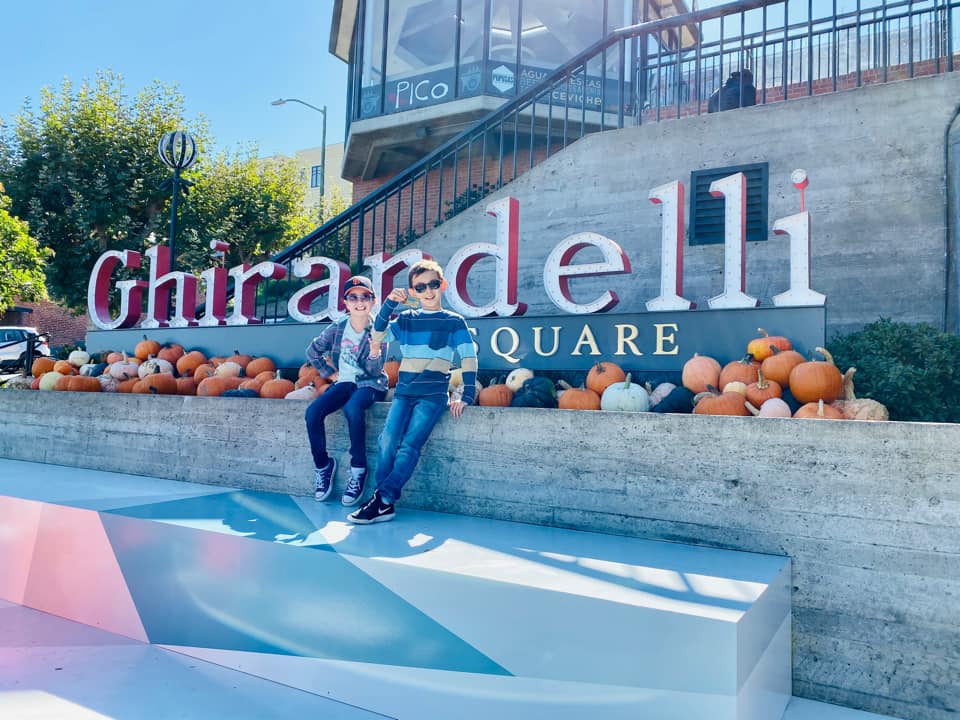 Two kids sit together near the sign for Ghirardelli in San Francisco.