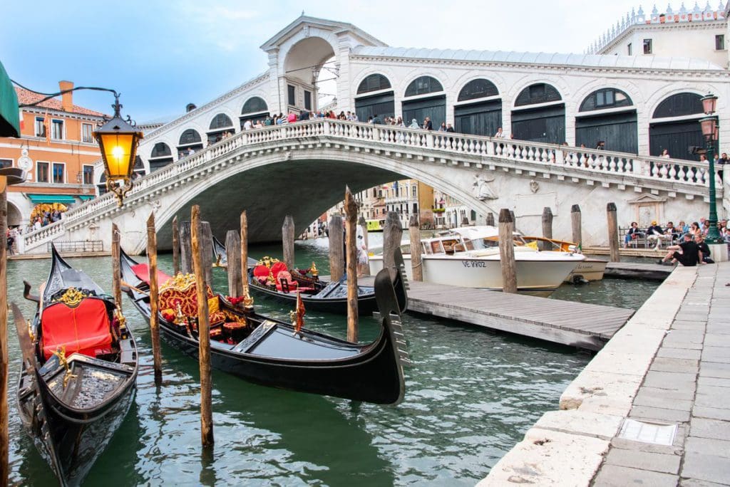 People stroll across the Rialto Bridge, while gondolas wait in the water below for new riders.