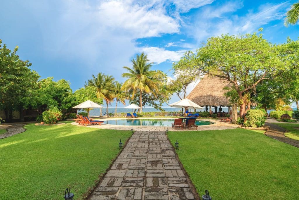 A path leads through a manicured lawn to the pool and surrounding pool deck at Turtle Inn in Belize.