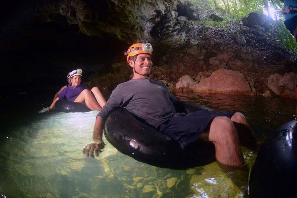 Two people on inner-tubes float through an underground river inside a cave near Ian Anderson's Caves Branch Jungle Lodge, one of the best Belize resorts for a family vacation.