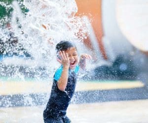 A young boy smiles as he splashes through a splash pad area.