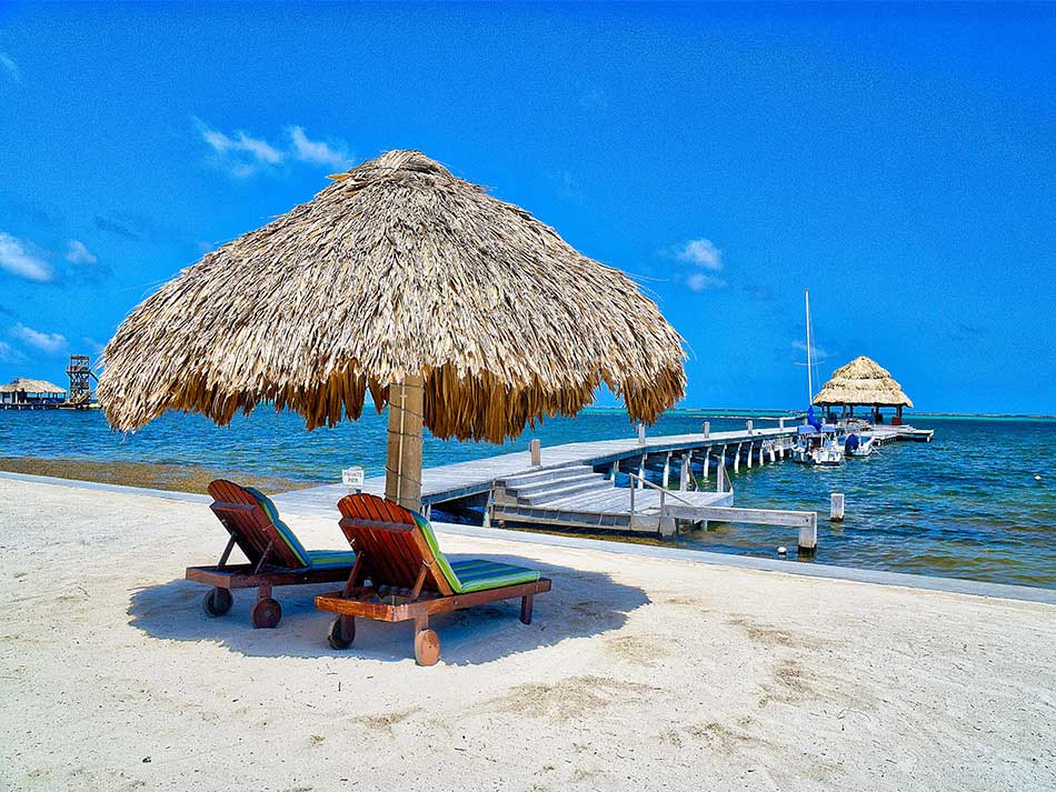 A cabana with two beach loungers sits along the beach at Xanadu Island Resort one of the best Belize resorts for a family vacation.
