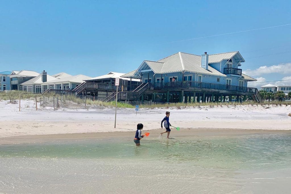 Two kids play in the water off-shore from a beach in 30A, with beach rentals on shore in the distance.