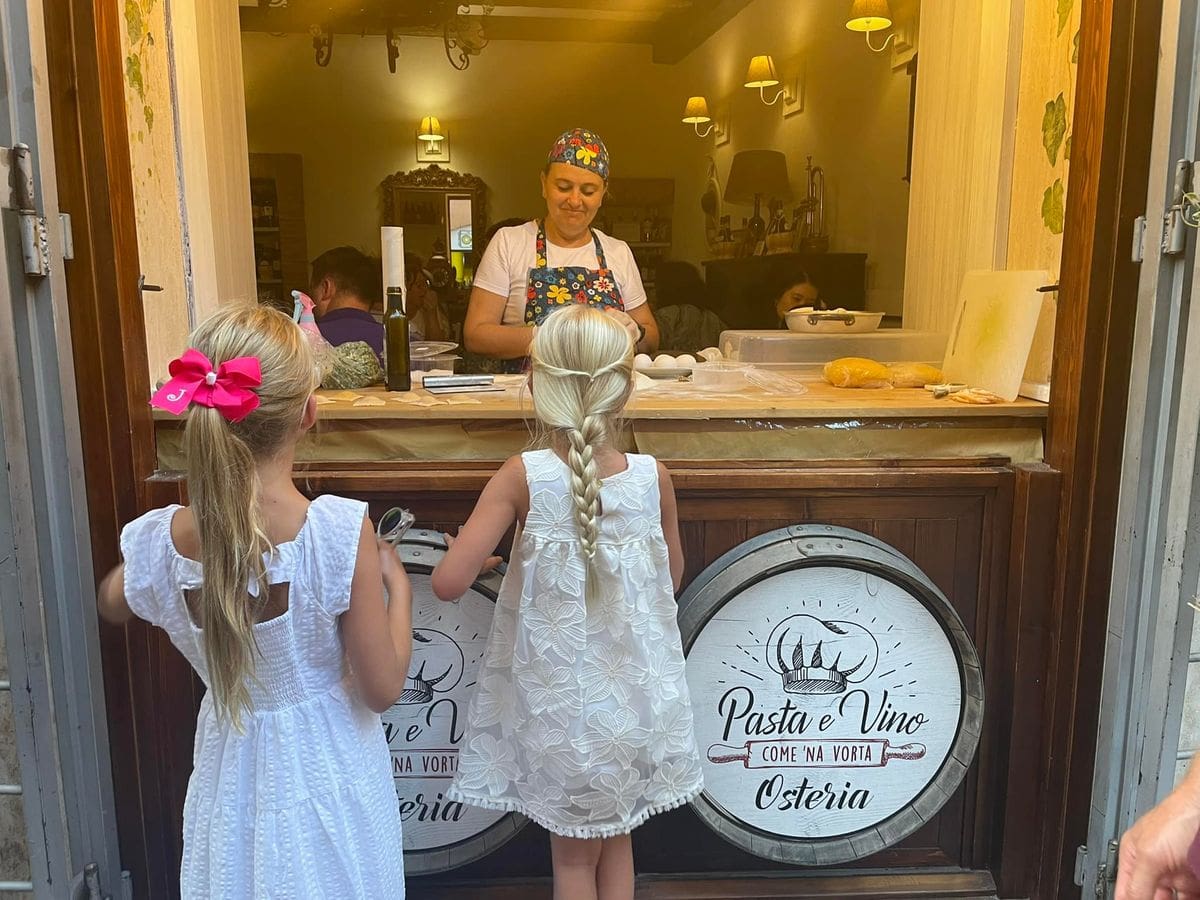 Two young girls watch a woman make pasta through a window at Pasta e Vino Osteria, one of the best restaurants in Rome for kids.