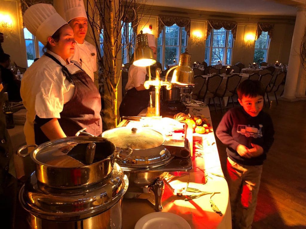 A young boy walks by a serving table with two staff members during Thanksgiving dinner at Mountain View Grand Resort and Spa, one of the best Thanksgiving destinations in the United States for families.
