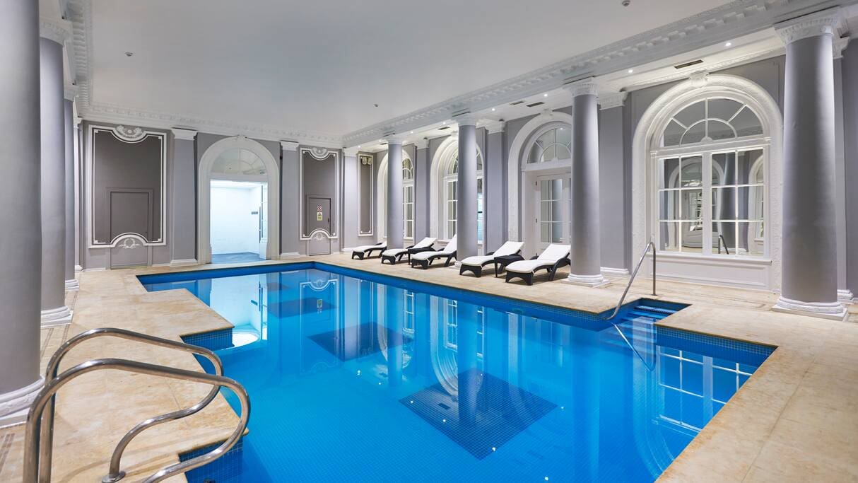 The pool and surrounding pool deck in a light and airy pool area within The Waldorf Hilton, London.