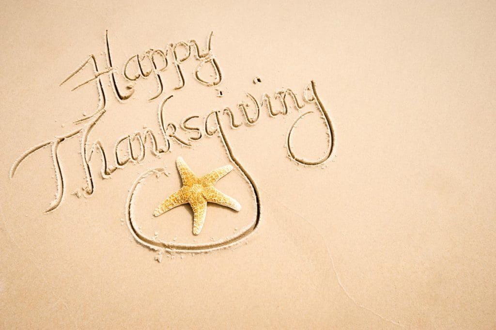 Happy Thanksgiving written in the sand on a beach, with a starfish hooked in the "g" of Thanksgiving.