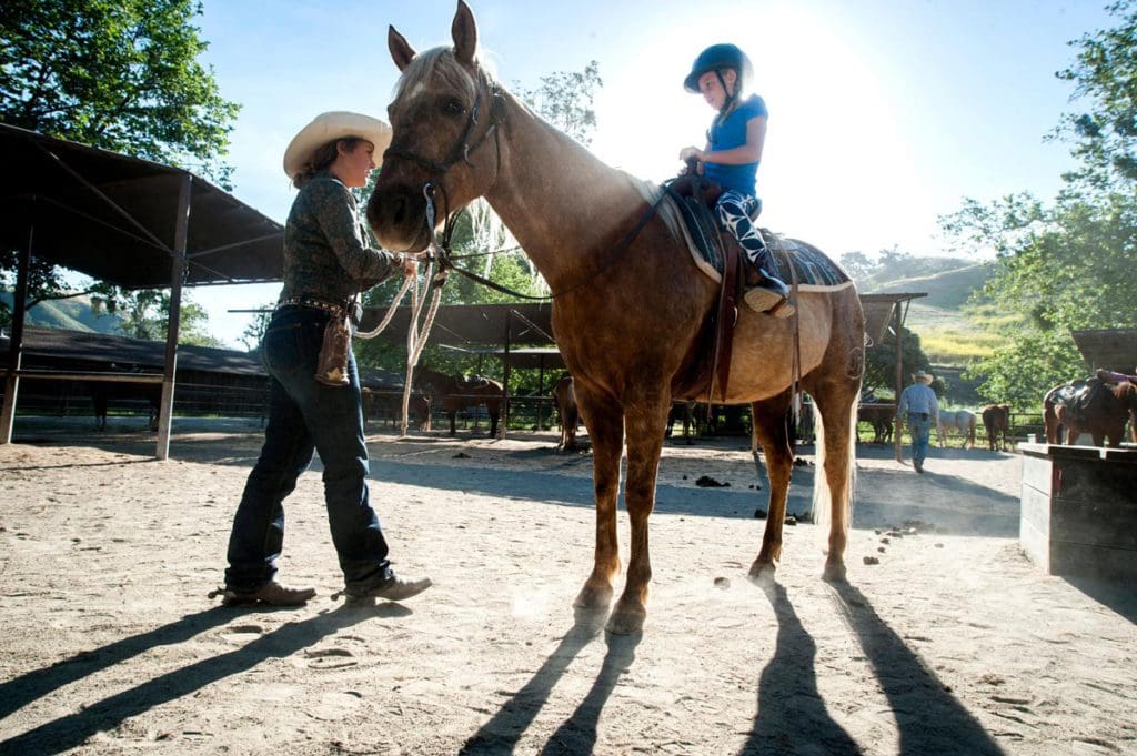 A staff member assists a young boy riding a horse within a horse pen at Alisal Guest Ranch and Resort.