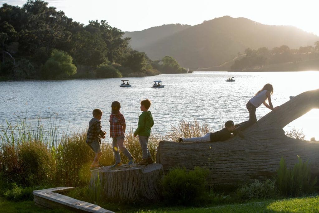 Several kids play near and on a large fallen log aside a lake at Alisal Ranch, one of the best all-inclusive hotels in the United States for families.