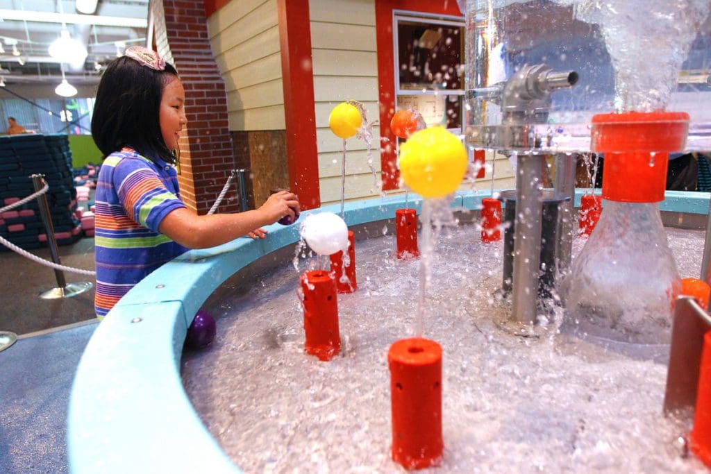 A young Asian girl plays in a water table exhibit at the Hands-On Museum in Ann Arbor, one of the best places to visit in Michigan with kids.