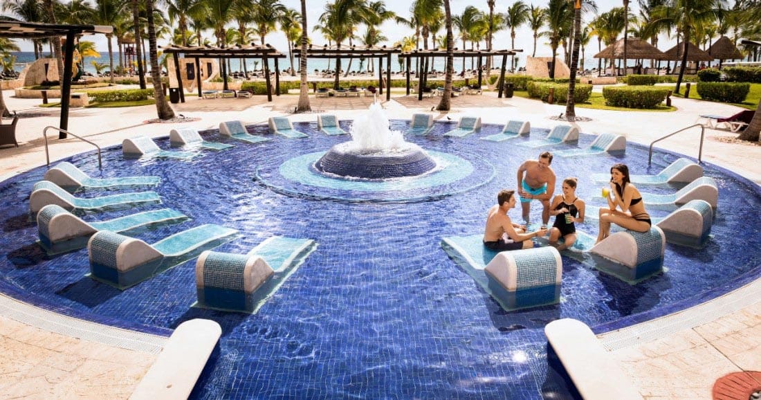 Four people hang out in a small pool with in-pool loungers at Barceló Maya Palace, one of the best resorts in Mexico with a water park for families.