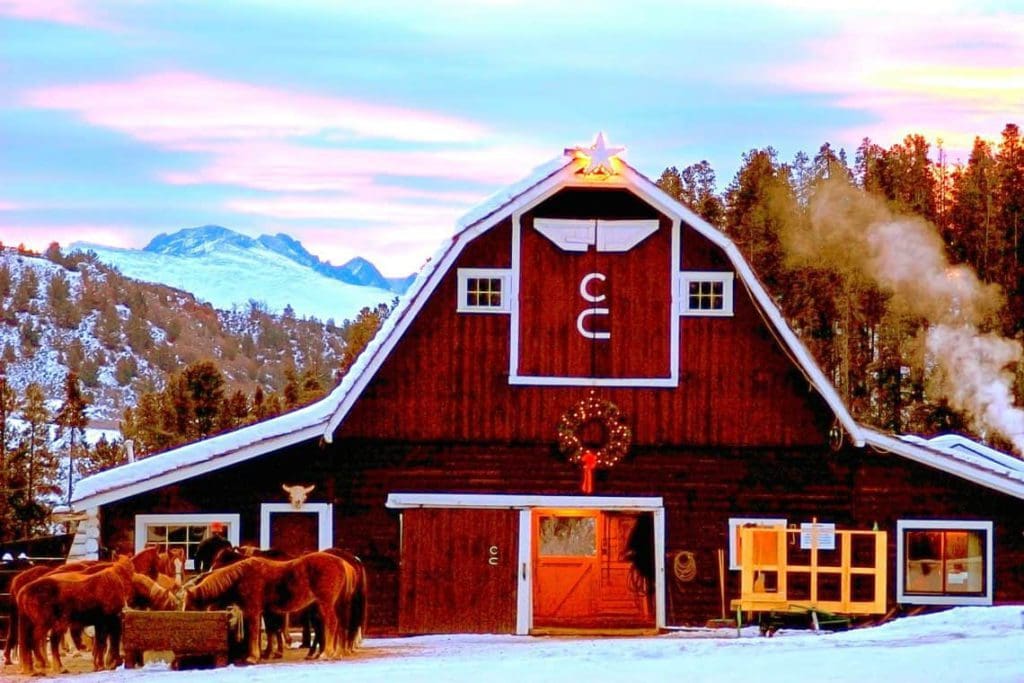 The exterior of the main barn at C Lazy U Ranch, decorated for Christmas, with horses out front.