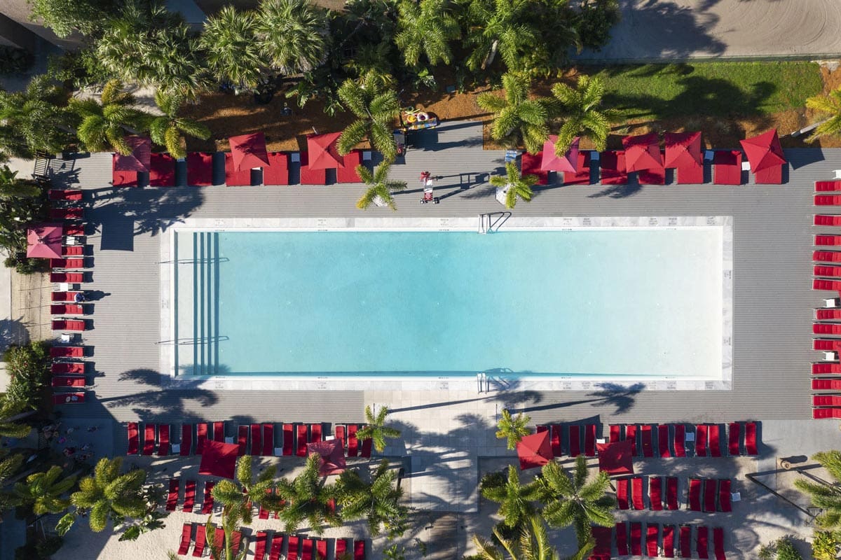 An aerial view of the pool and surrounding pool deck, featuring bright red umbrellas, at Club Med Sandpiper Bay.