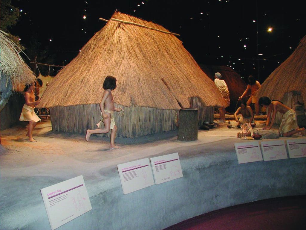 An interactive exhibit featuring models of young Native American kids running around a rustic home at the Cahokia Mounds State Historic Site, one of the best places to visit in Southern Illinois for families.