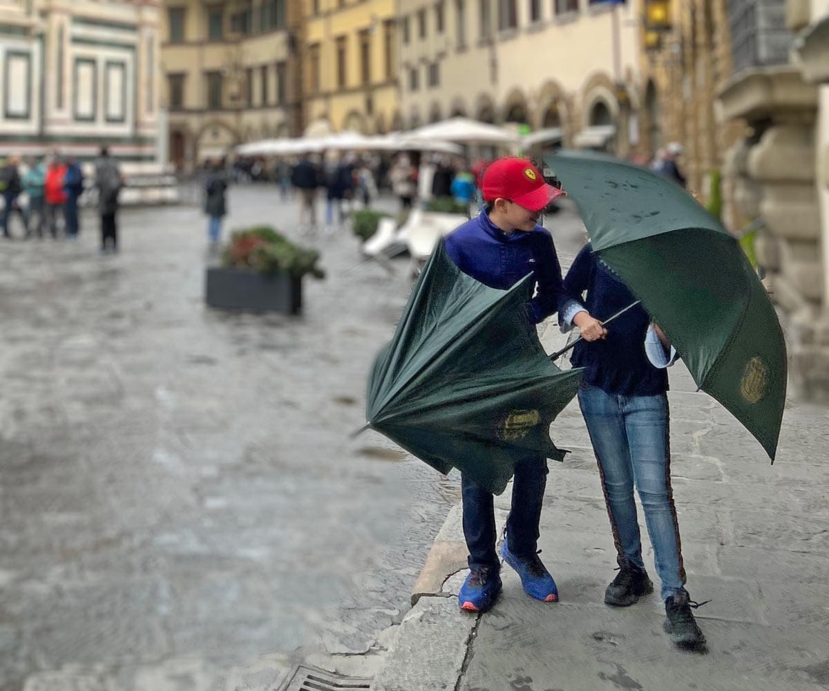 Two kids walk along a street in Florence with umbrellas on a rainy day.