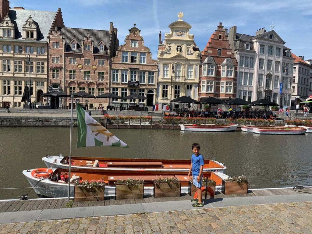 A young boy stands next to a boat along a canal in Ghent, one of the best places in Belgium for families.