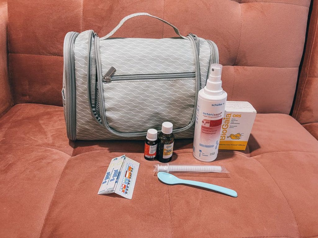 A small medical kit sits on a couch waiting to be packed for a European family vacation with toddlers.