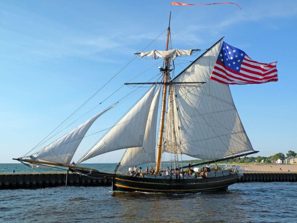 A ship with large sails goes down a body of water in Michigan, as part of the Michigan Maritime Museum, one of the best places to visit in Michigan with kids.