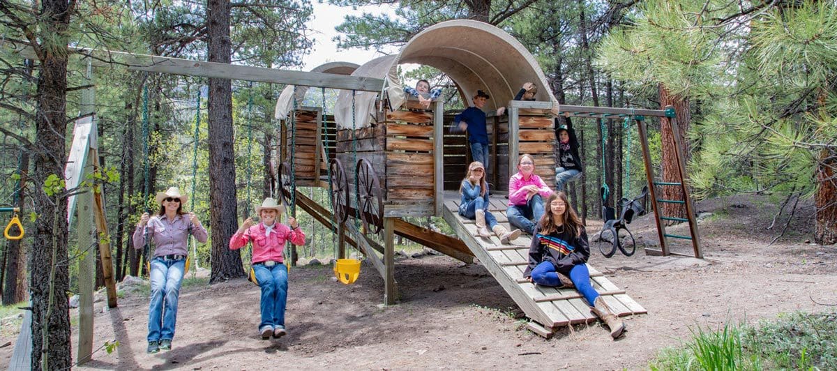 A large family poses for a picture in a staged covered wagon at Rainbow Trout Ranch, one of the best all-inclusive hotels in the United States for families.
