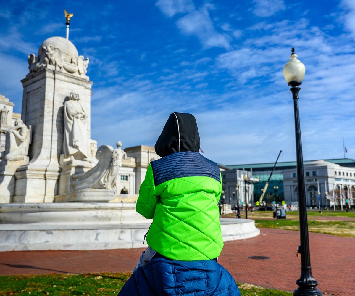 A toddler sits atop his parent's shoulders, while looking at a monument in DC.