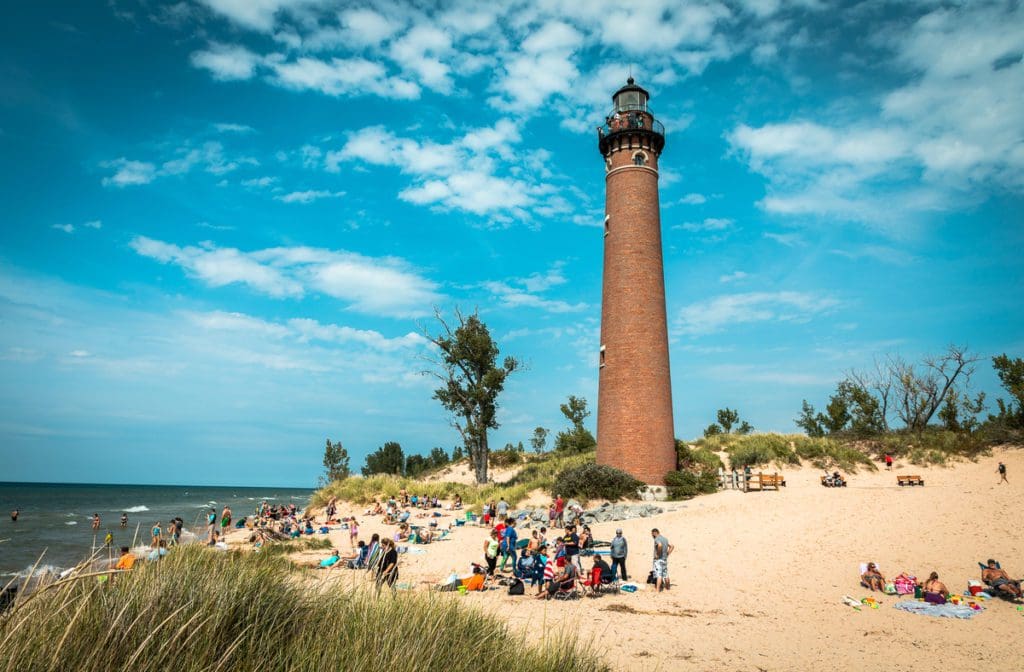Families explore the area below a lighthouse along a beach in Michigan, called Silver Lake Sand Dunes, one of the best places in Michigan to visit with kids.