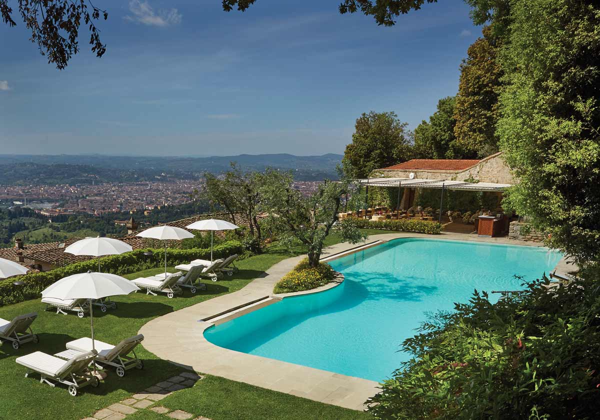 The outdoor pool and surrounding green space, including white umbrellas and loungers, at Belmond Villa San Michele.