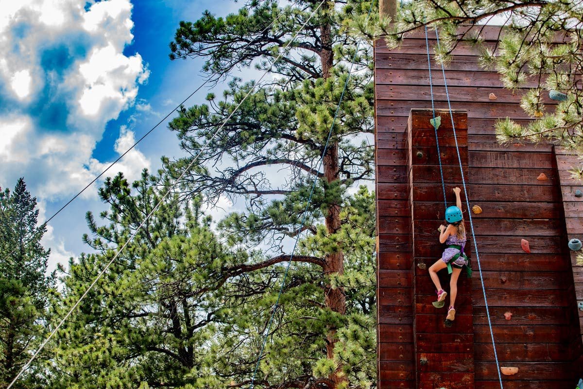 A young girl climbs an outdoor climbing tower at YMCA of the Rockies, one of the best all-inclusive hotels in the United States for families.