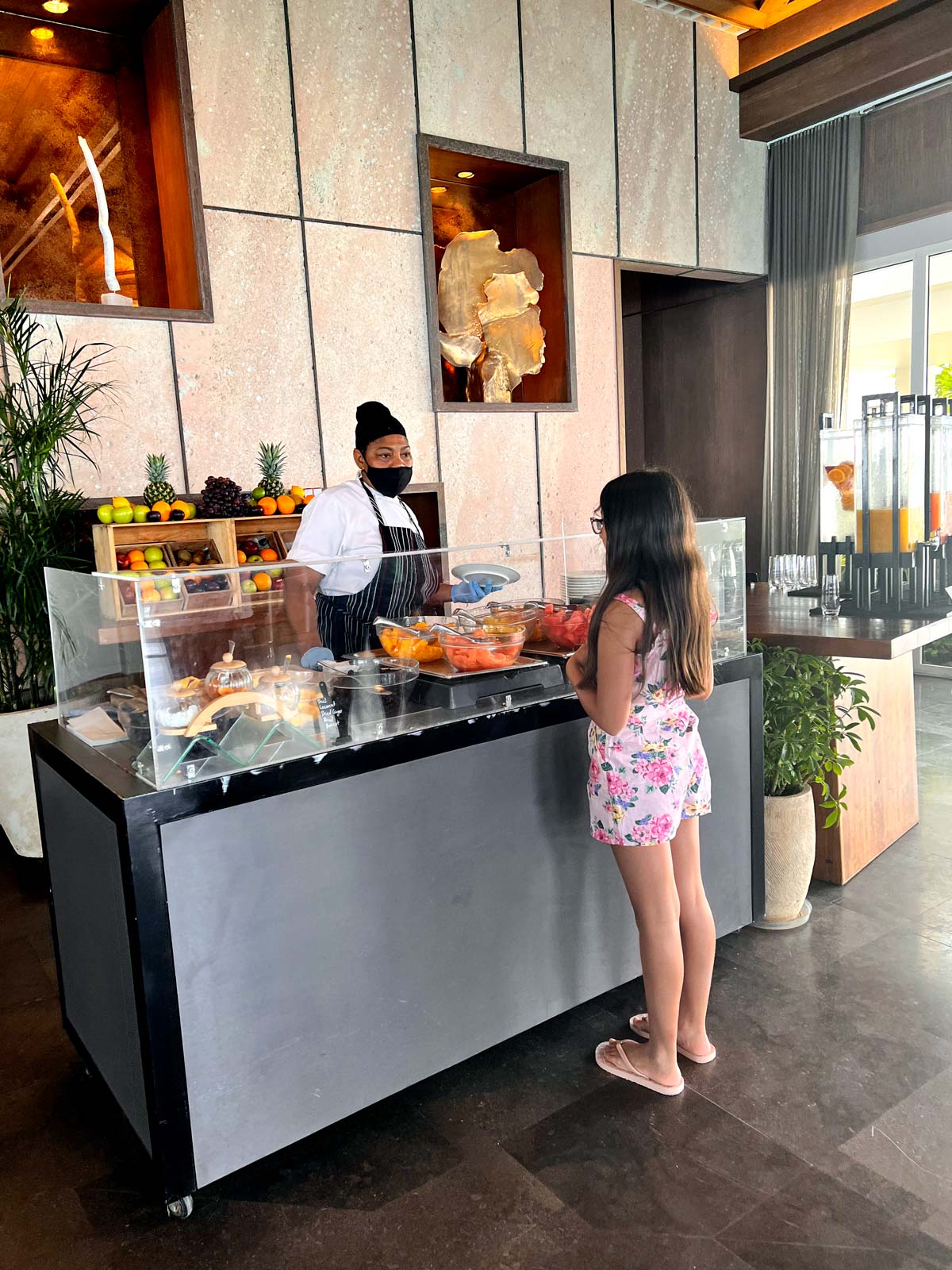 A young girl retrieves buffet breakfast items with staff help.