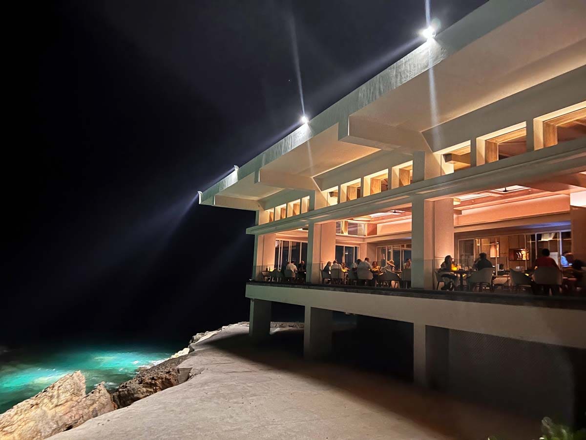 A restaurant perched along the ocean lights up at night.