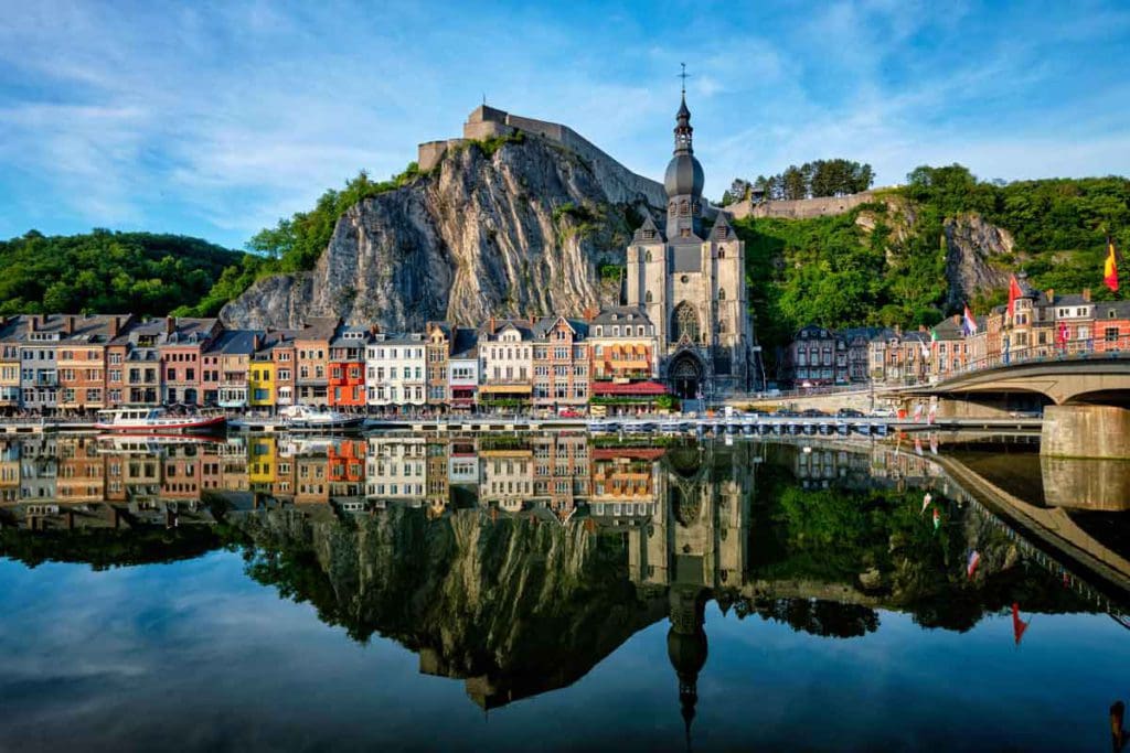 A charming view of colorful buildings along the water's edge in Dinant, one of the best places in Belgium for families.