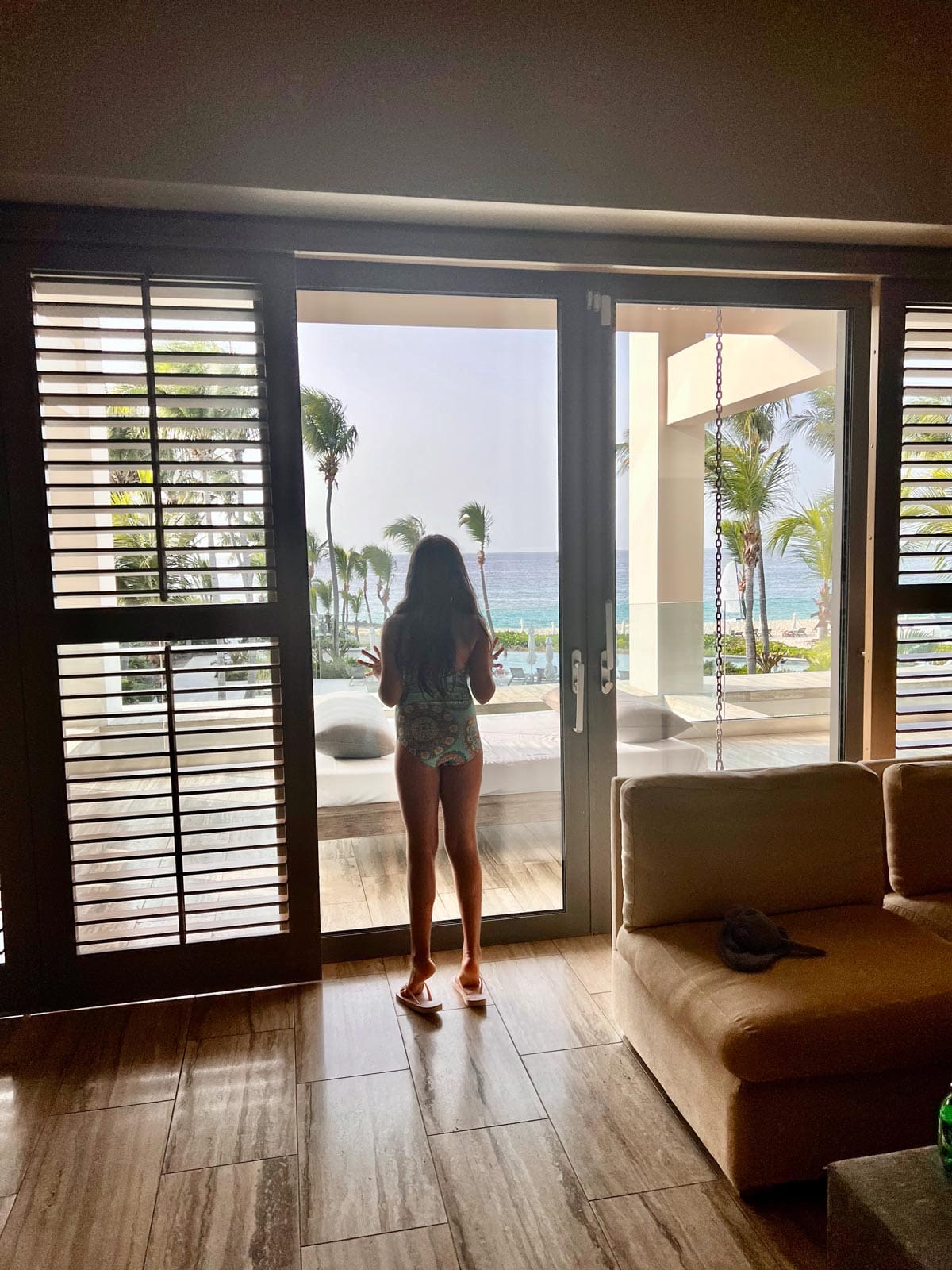 A young girl looks out the patio doors of a luxury suite at Four Seasons Resort and Residences Anguilla onto the ocean.
