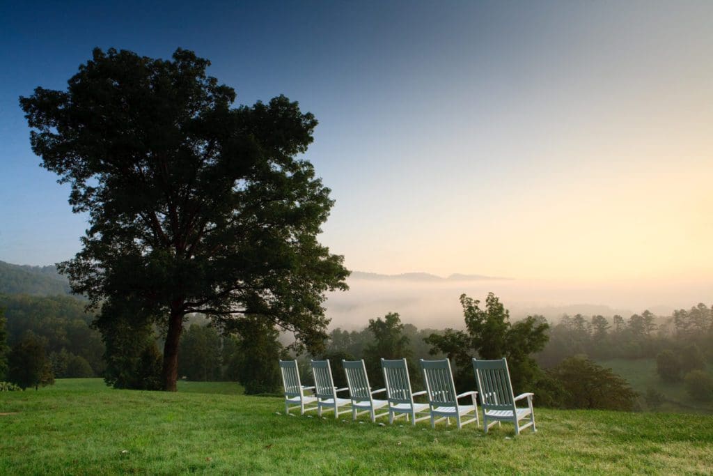Several white chairs sit on a hillside overlooking a scenic view of a valley in Tennessee on Blackberry Farm.