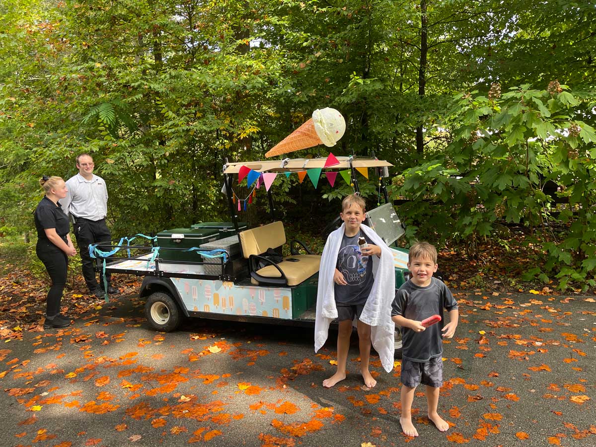 Two kids stand in front of an ice cream golf cart, while on a family getaway to Blackberry Farm in Tennessee, with two staff members standing nearby.