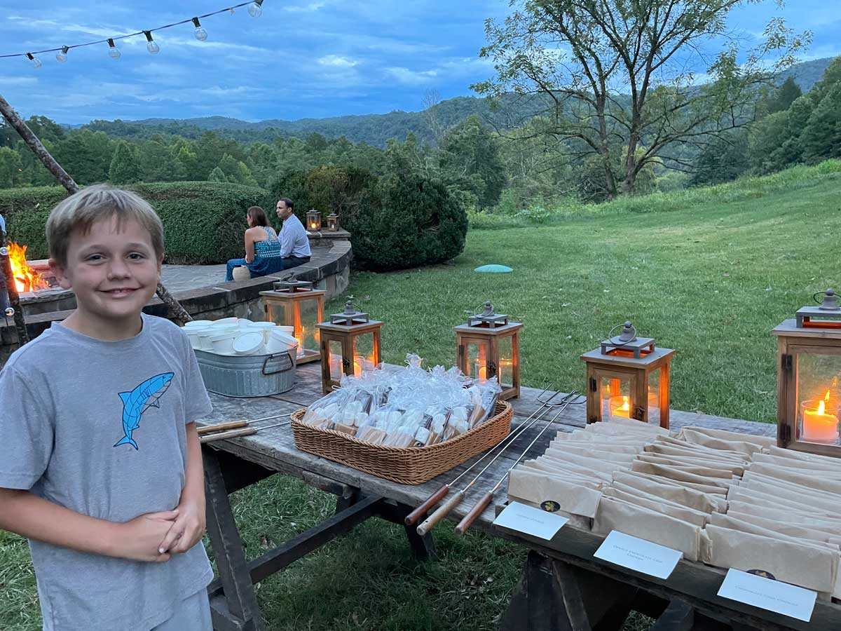 A young boy stands in front a picnic table filled with s'mores supplies.